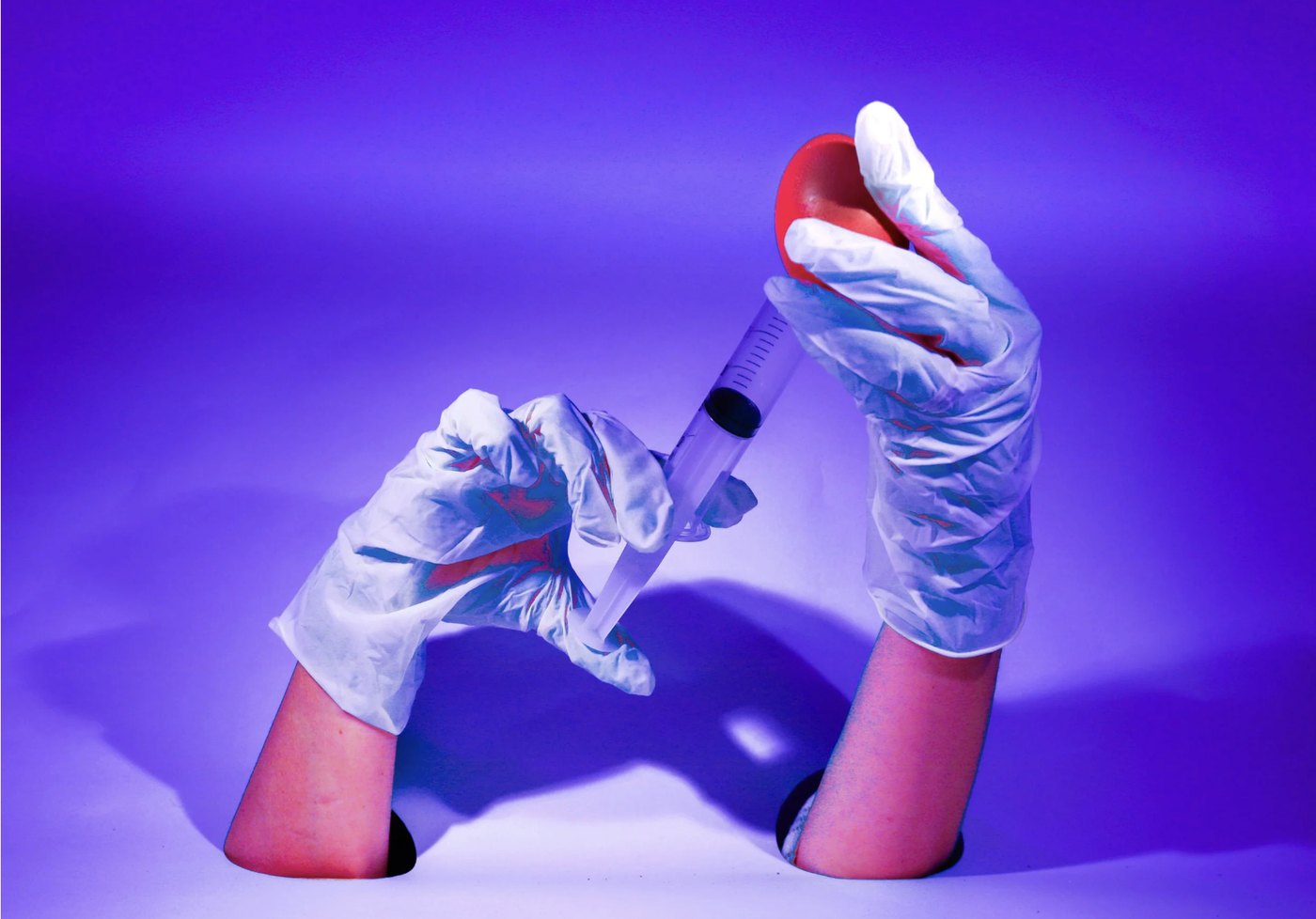 Gloved hands with a syringe and a red fruit under violet light