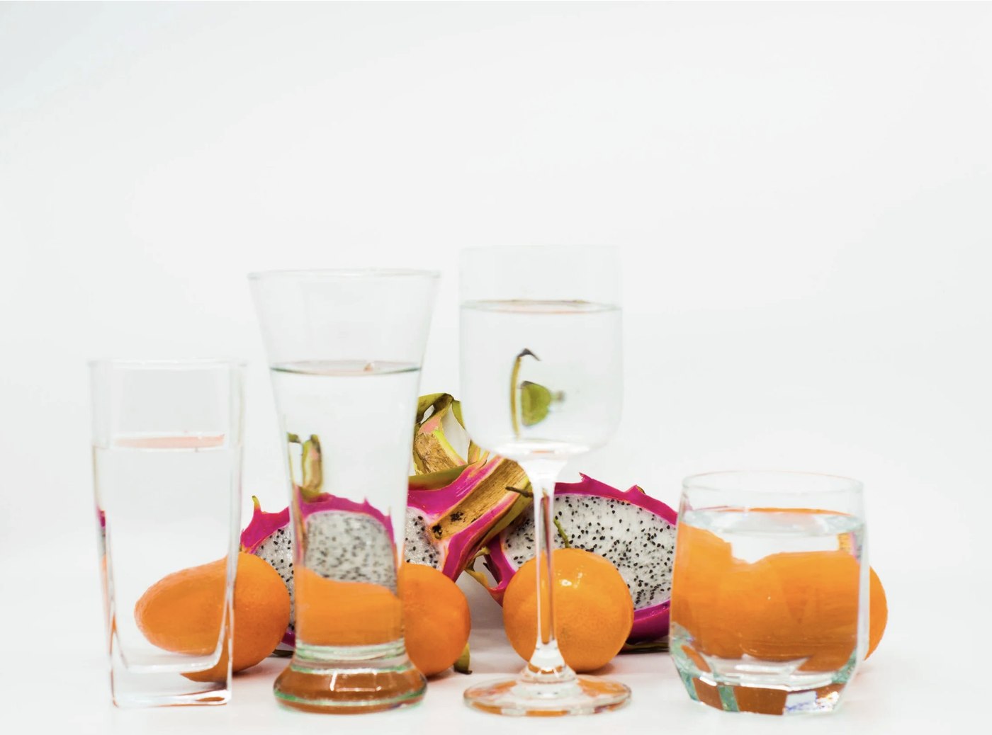 Dragon fruit and oranges seen through glasses of water